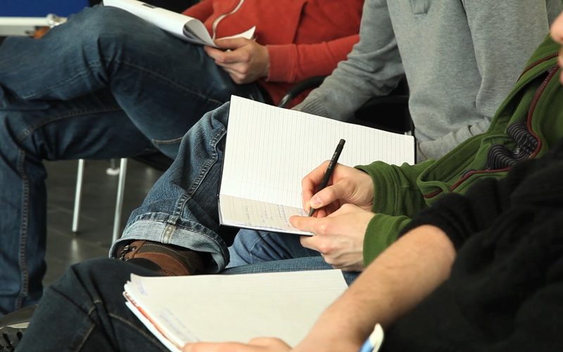 Teilnehmende machen sich Notizen auf Schreibblöcken
